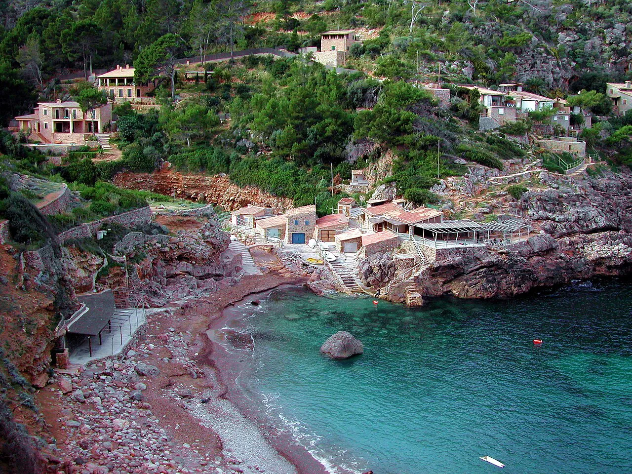 Turquoise water and a pebble beach in the rocky cove of Cala de Deià below terraced hillsides