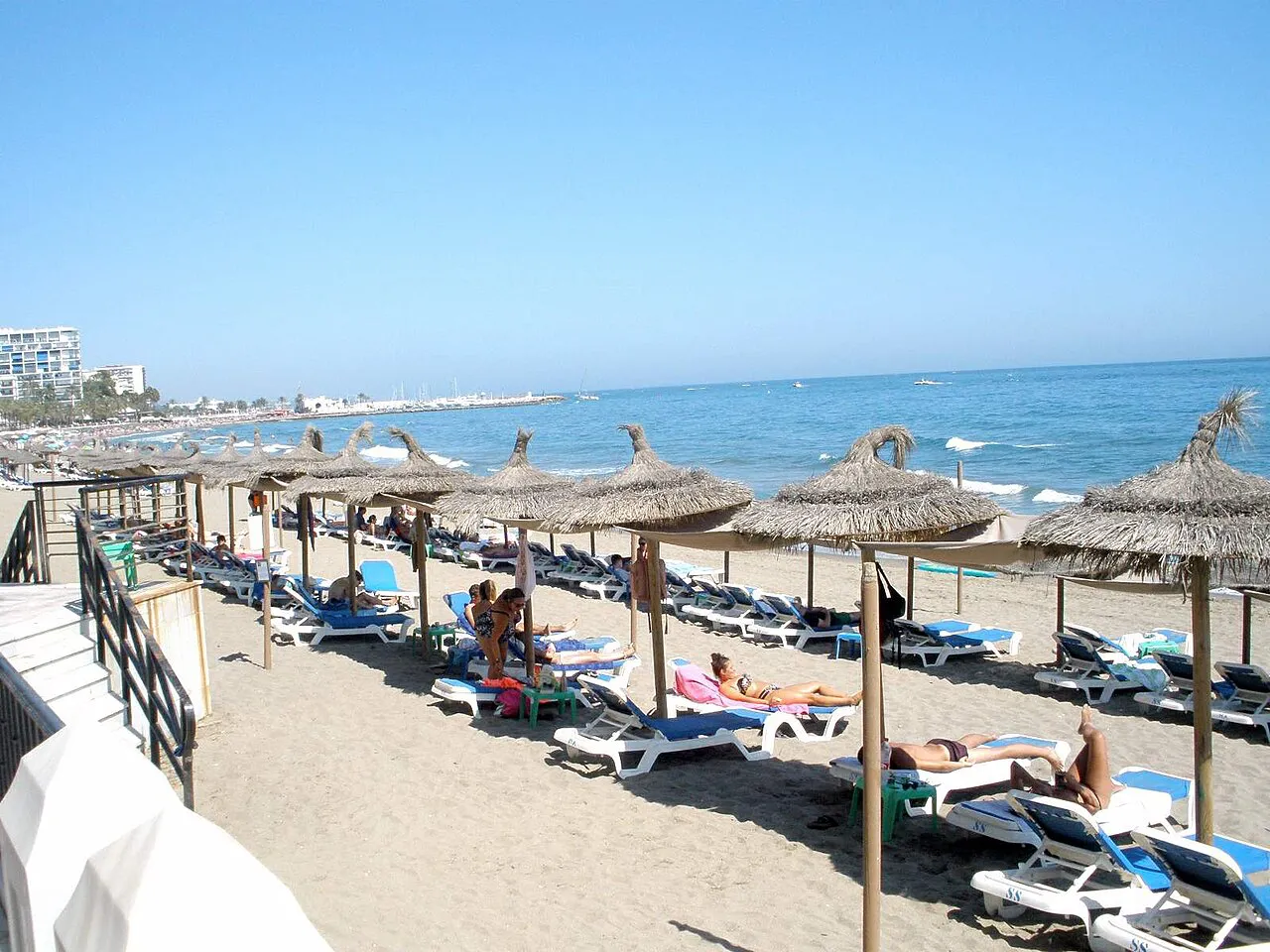 Rows of thatched parasols and sun loungers on Playa de la Fontanilla in Marbella beside a calm sea