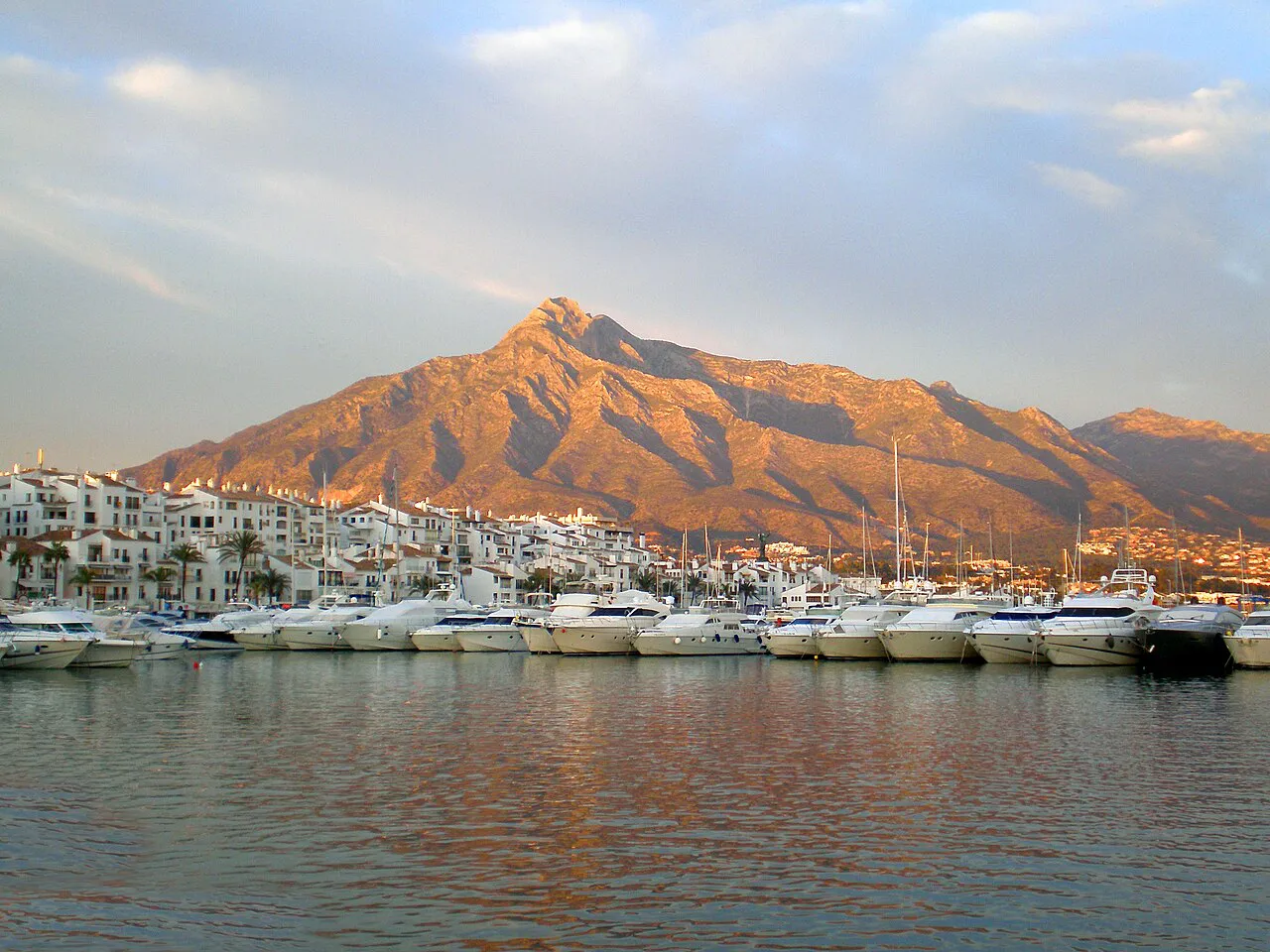 Moored yachts in Puerto Banús marina with La Concha mountain glowing in the evening light behind