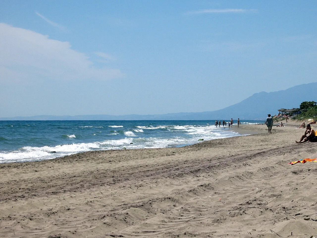 Long natural sandy beach at Artola-Cabopino in Marbella with surf and mountains along the coast