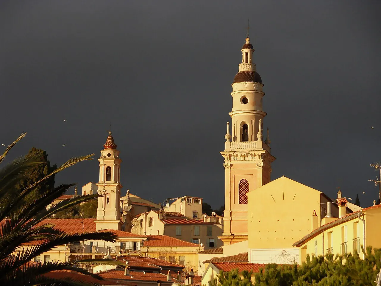 Bell tower of the Basilica of Saint-Michel glowing in evening sun above the old town rooftops of Menton