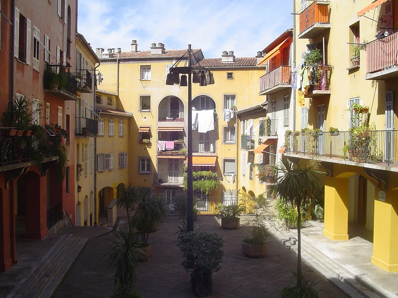 Small square in Vieux Nice framed by ochre and yellow houses with balconies and potted plants