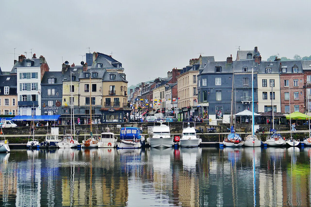 Tall slate-fronted houses reflected in the Vieux Bassin harbour at Honfleur, lined with moored boats
