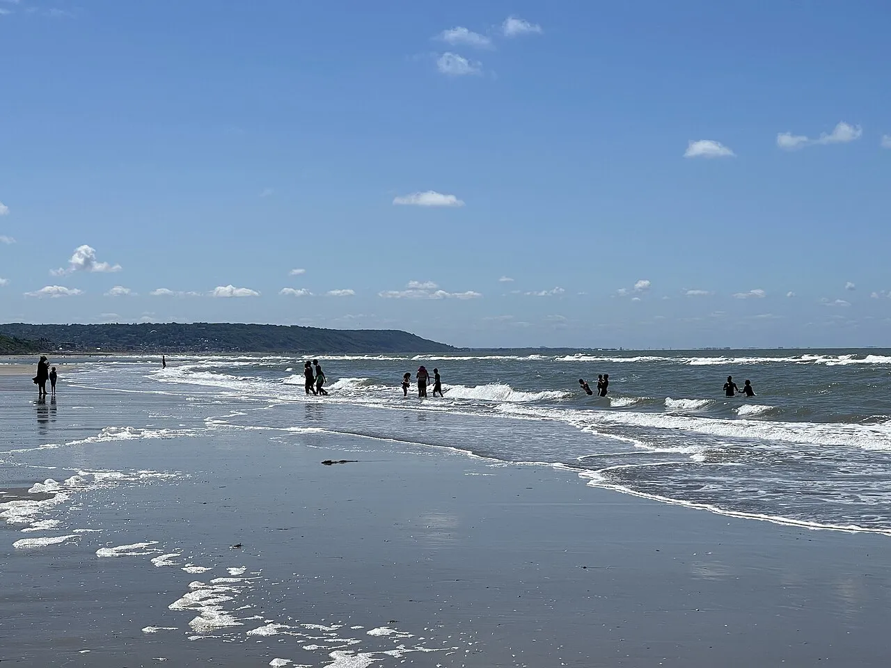 Wide sandy beach at Deauville with gentle waves and wooded headland in the distance