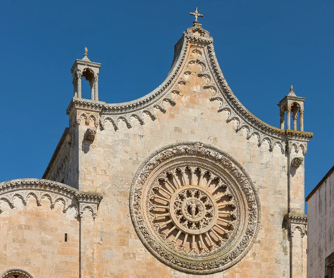 Gothic facade and carved rose window of Ostuni Cathedral against a deep blue sky
