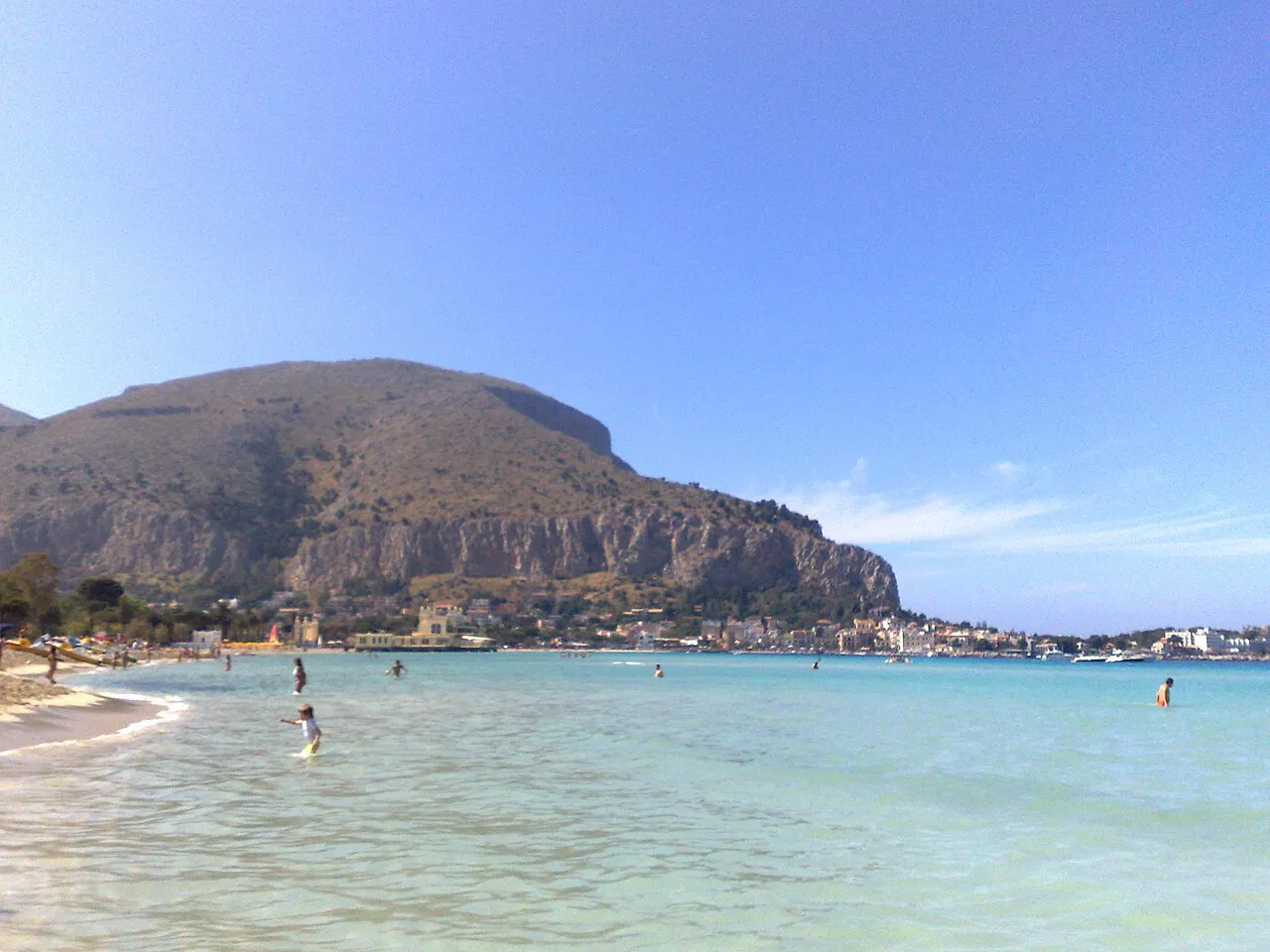 Turquoise shallow water at Mondello beach below a rocky headland, Palermo