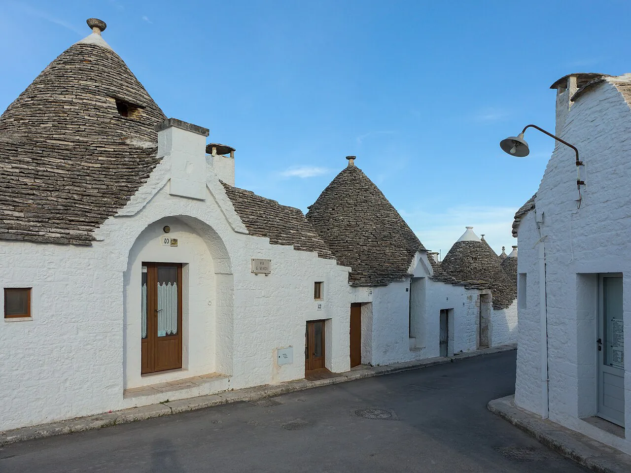 Whitewashed trulli with conical stone roofs along a quiet street in Alberobello’s Rione Aia Piccola