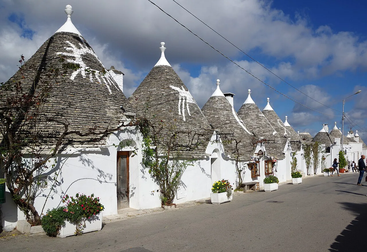 A row of whitewashed trulli with painted symbols on their conical roofs along a street in Alberobello
