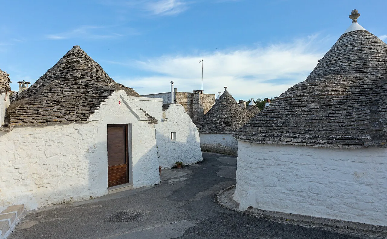 Whitewashed trulli with grey conical stone roofs on a quiet street in Alberobello’s Rione Aia Piccola