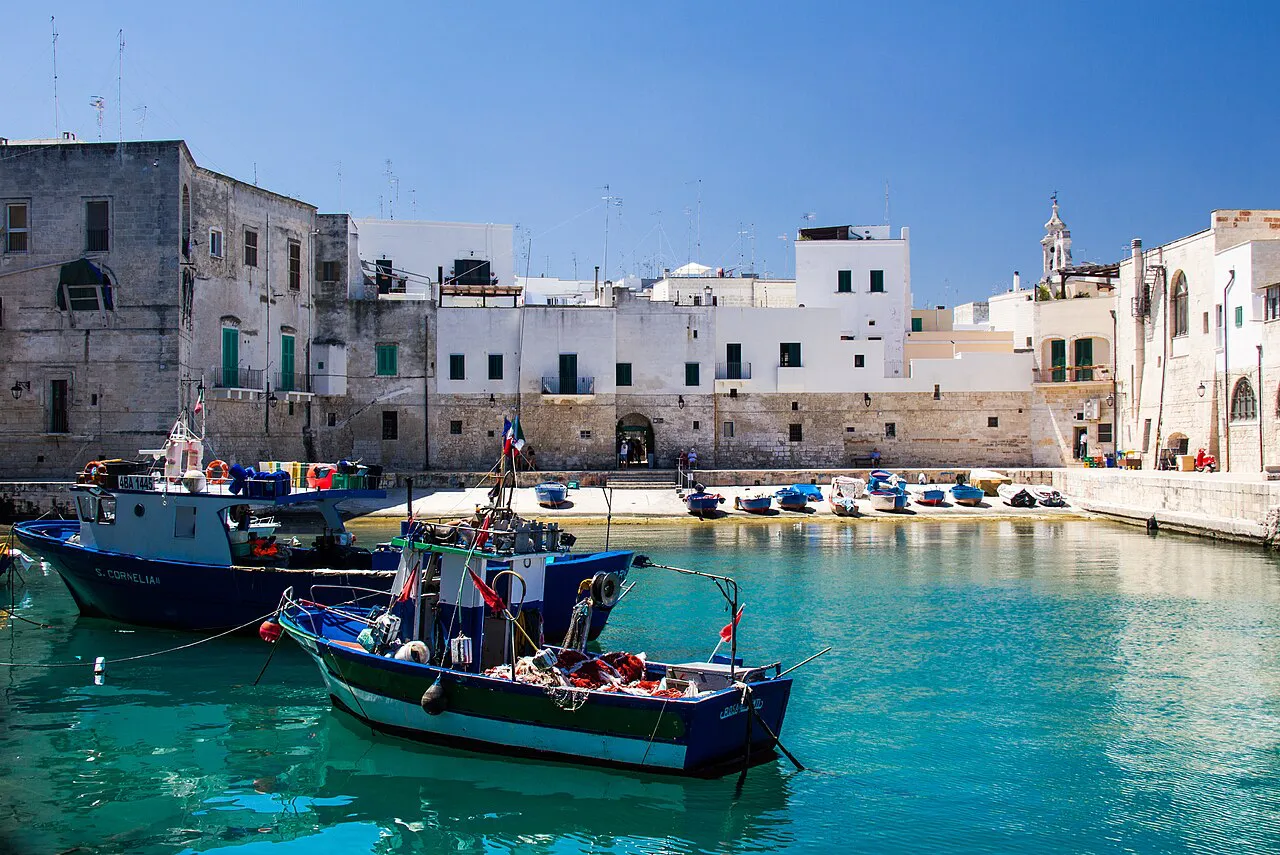 Blue fishing boats on turquoise water in Monopoli’s old harbour below pale stone buildings