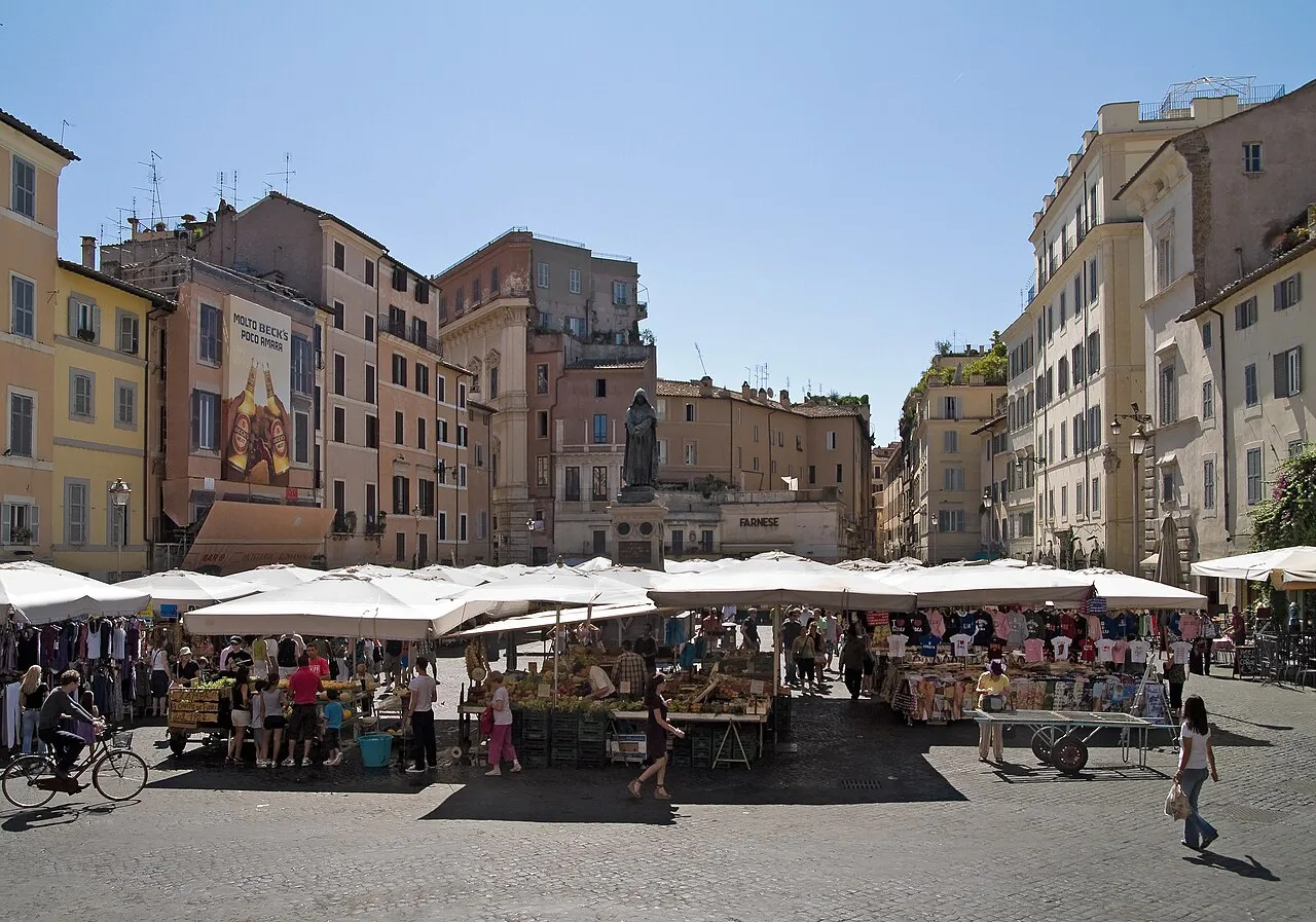 Market stalls under white umbrellas in Campo de' Fiori, Rome, ringed by old pastel buildings