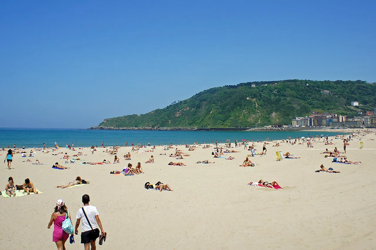 Wide sandy Zurriola beach in Gros on a sunny day, with green Monte Ulia rising behind, San Sebastián