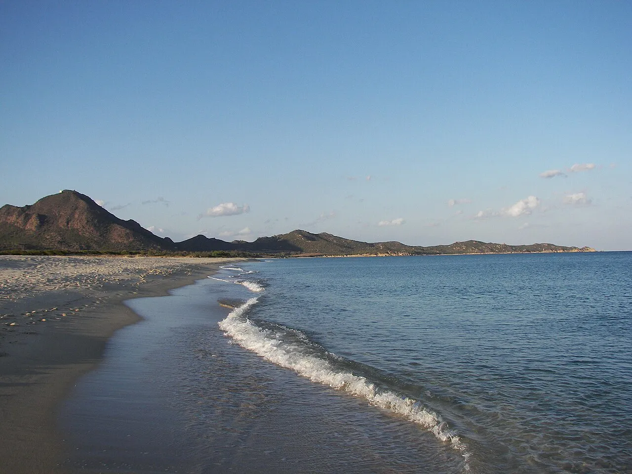 Gentle waves on the long sandy beach at Costa Rei with low mountains along the coast