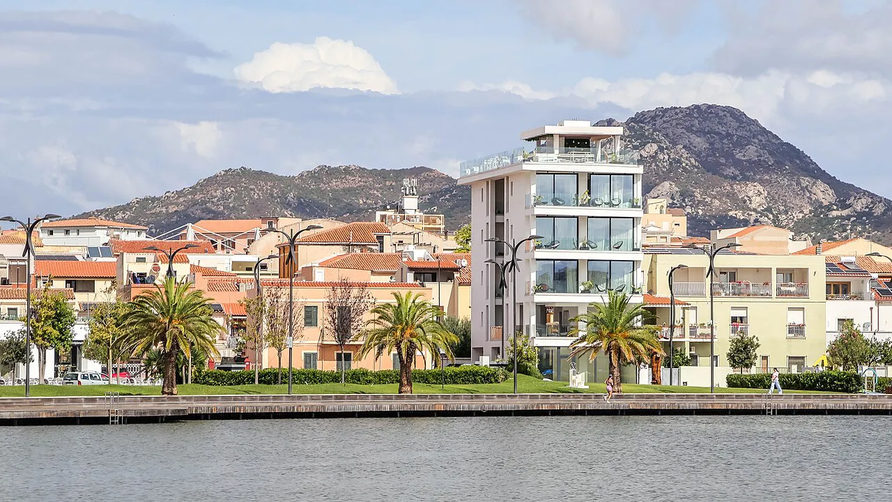 Olbia's waterfront promenade with palm trees and apartment buildings in front of rocky hills