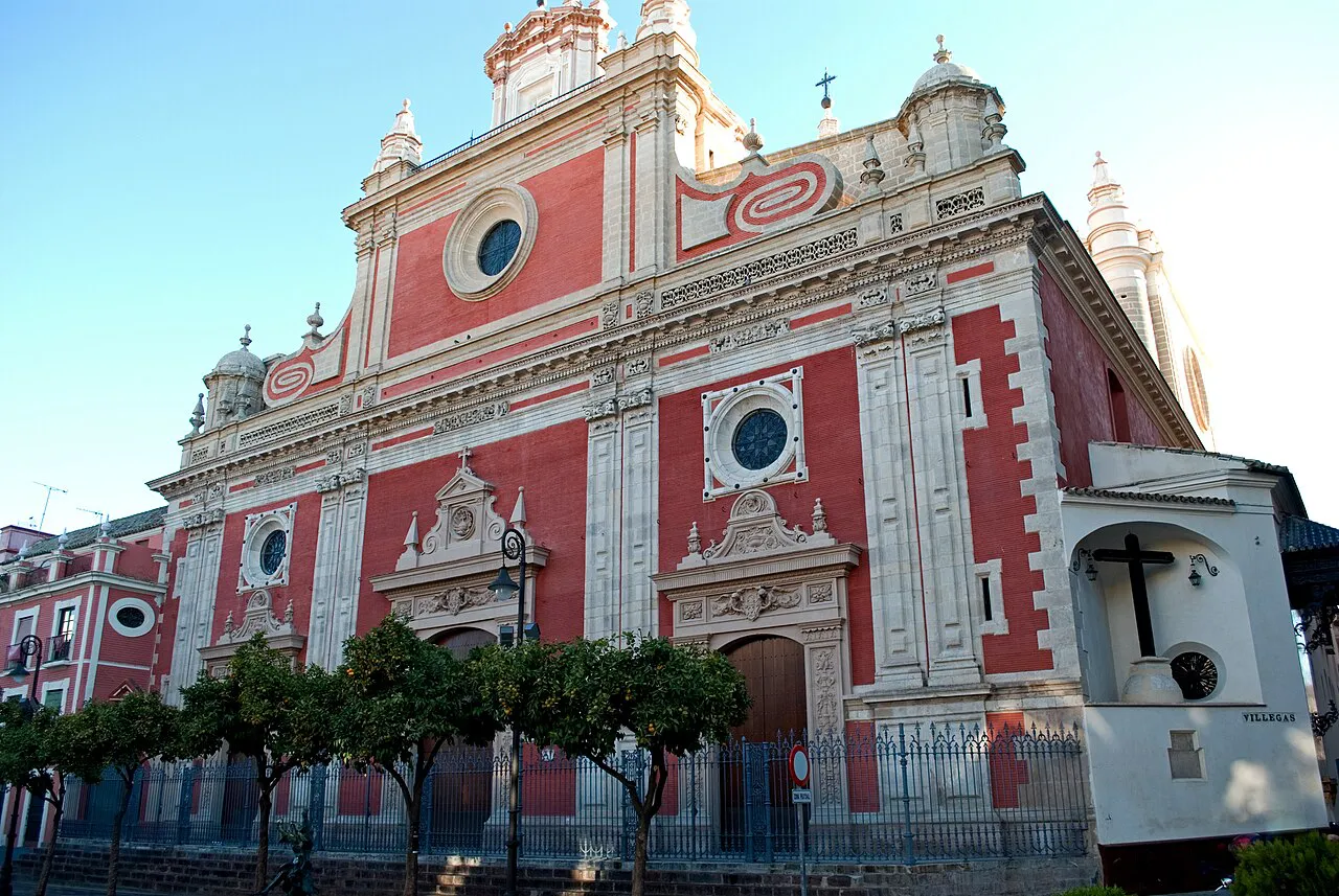 The red and cream baroque facade of the Iglesia del Salvador above orange trees, Seville