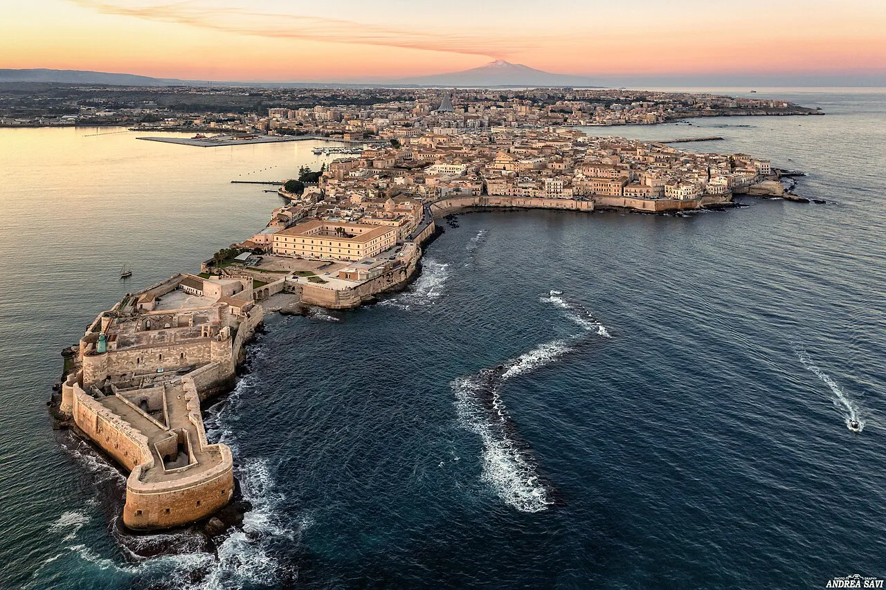 Aerial view of Ortigia island in Siracusa at sunset, with Castello Maniace at its tip and Etna beyond