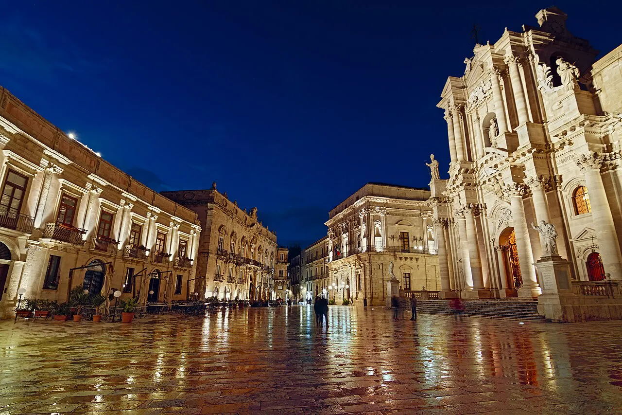 Piazza Duomo in Ortigia, Siracusa, at blue hour with the floodlit baroque cathedral facade and wet paving