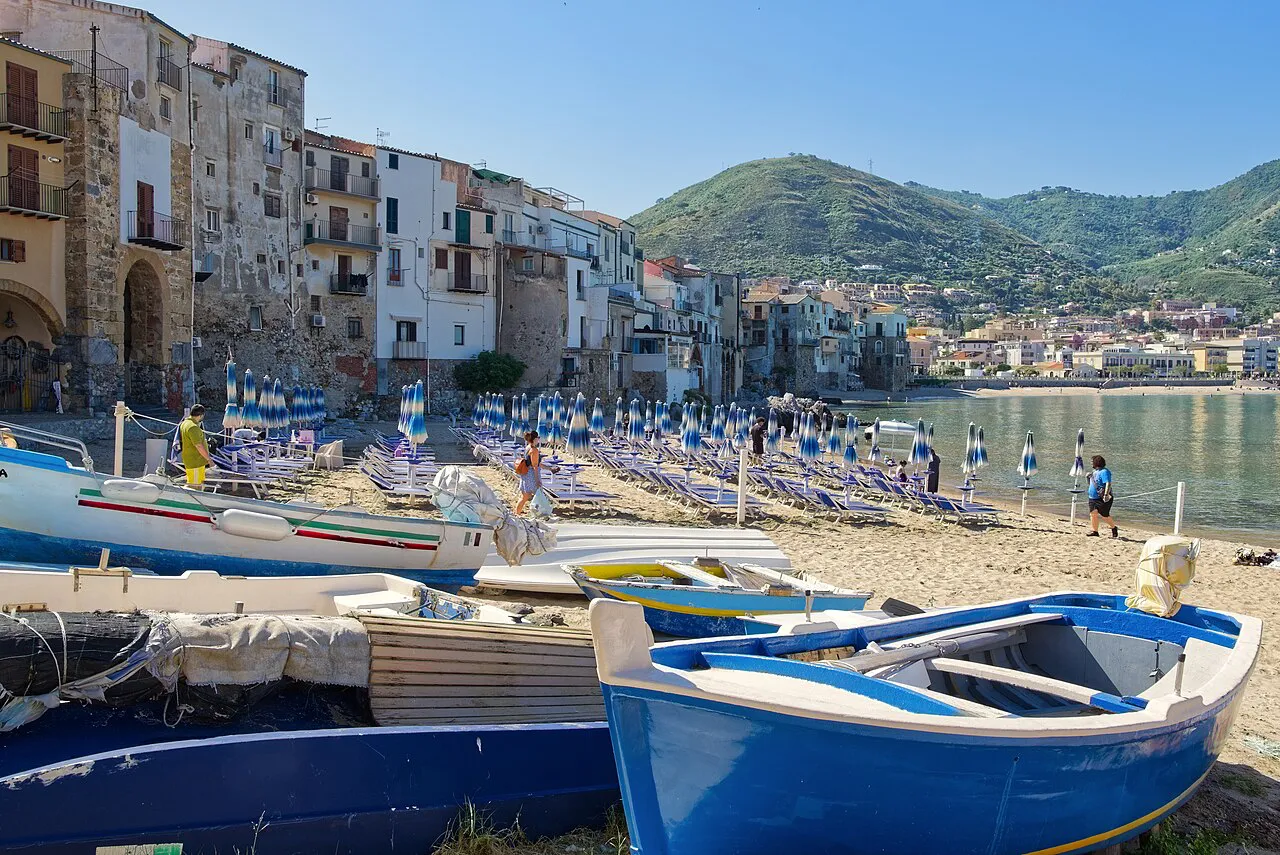 Fishing boats on the sand below the old seafront houses of Cefalù’s Porto Vecchio, with green hills behind