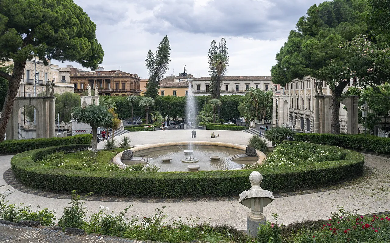 Circular fountain, clipped hedges and tall pines in the Villa Bellini public garden, Catania