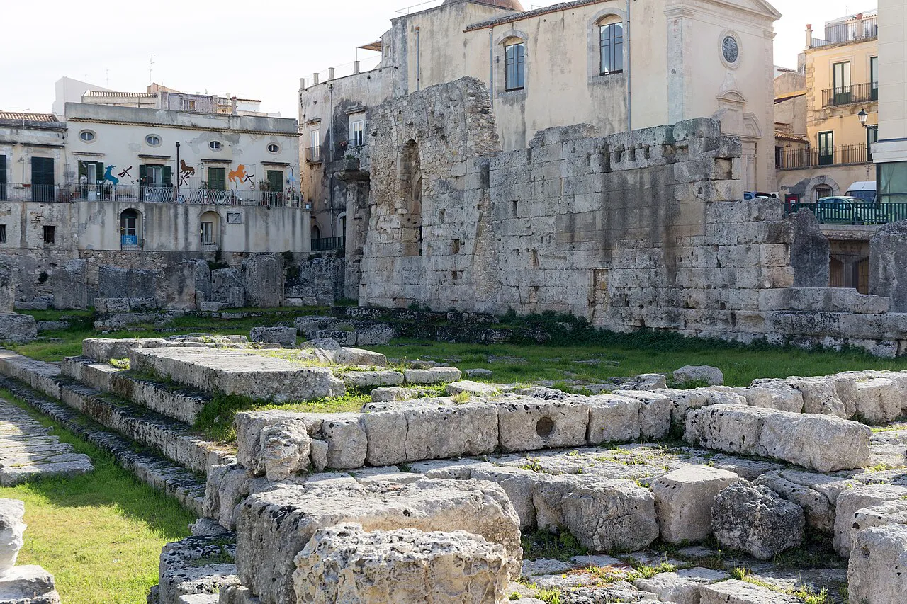 Ruined columns and stone blocks of the Temple of Apollo in Ortigia, framed by old buildings