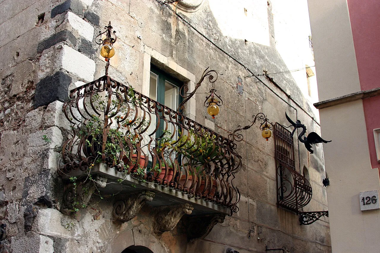 Ornate wrought-iron balcony on an old stone building along Corso Umberto, Taormina