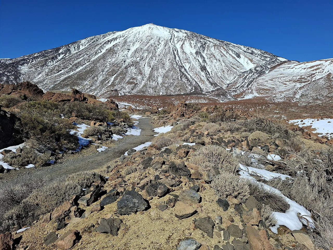 Snow-capped Mount Teide above a rocky volcanic landscape dusted with snow in Teide National Park, Tenerife