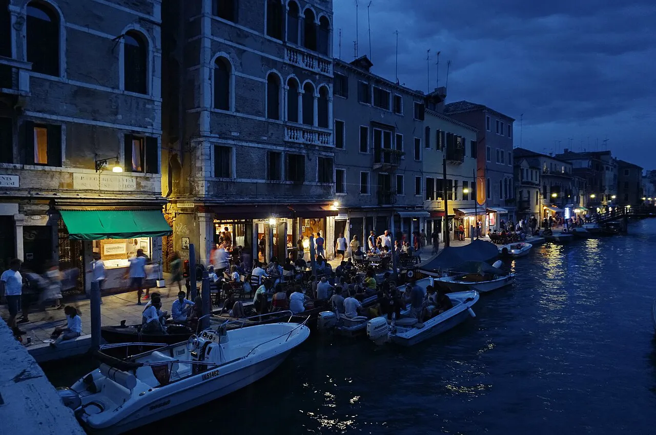 Fondamenta degli Ormesini in Cannaregio, Venice, at dusk with lit canalside terraces and moored boats